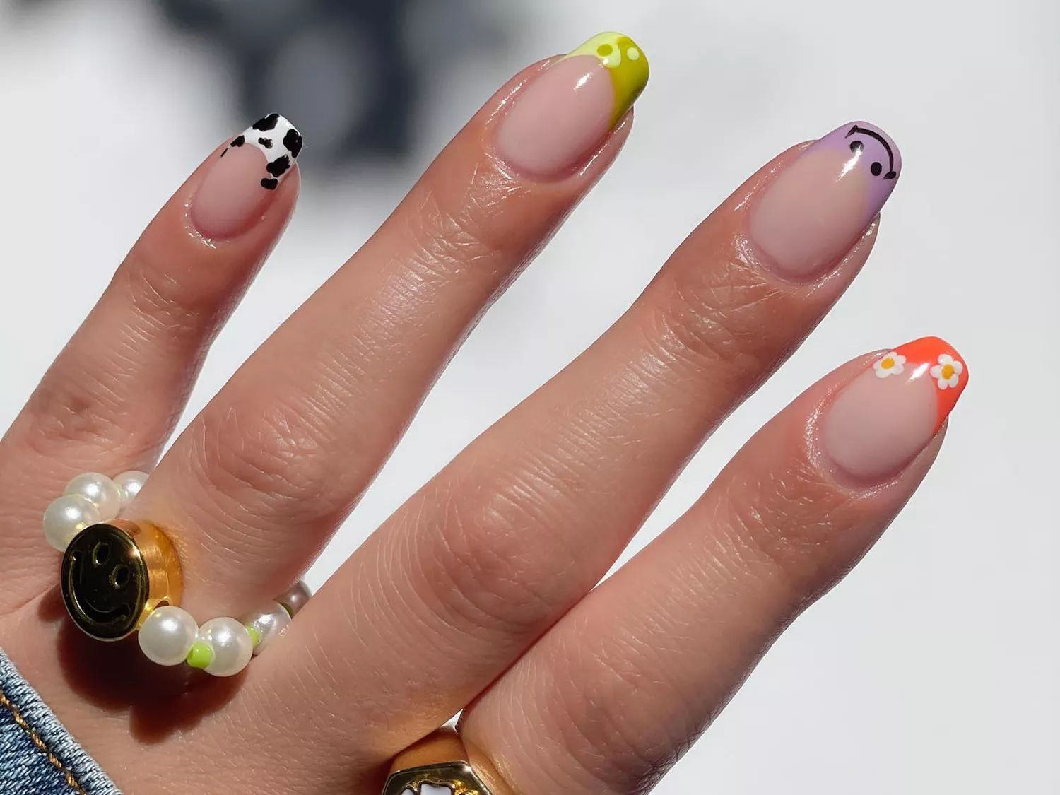 Mismatched French tip manicure with smiley, daisy, yin/yang, and cow print designs