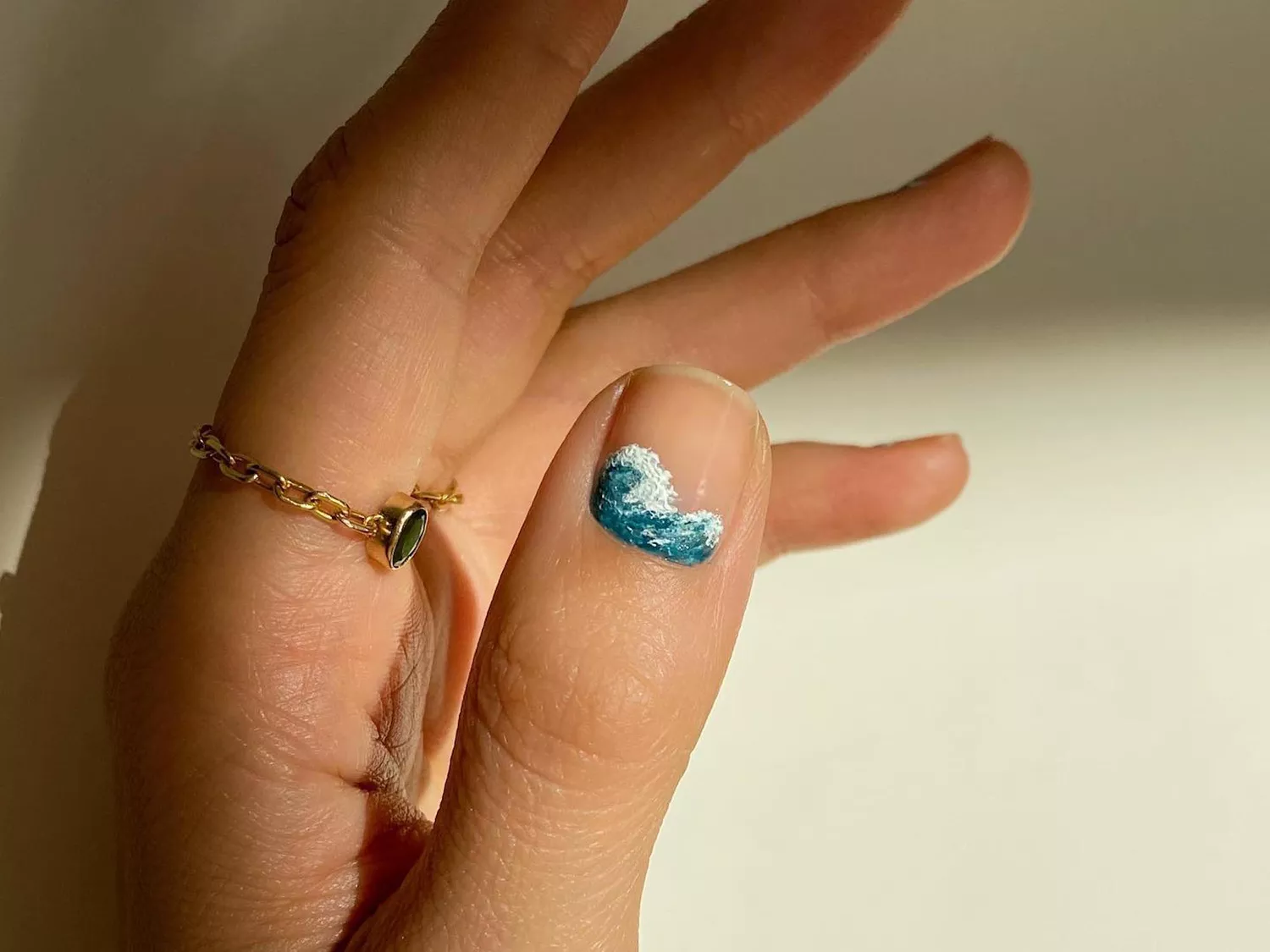 Manicure with neutral base and intricate ocean wave design on thumbnail