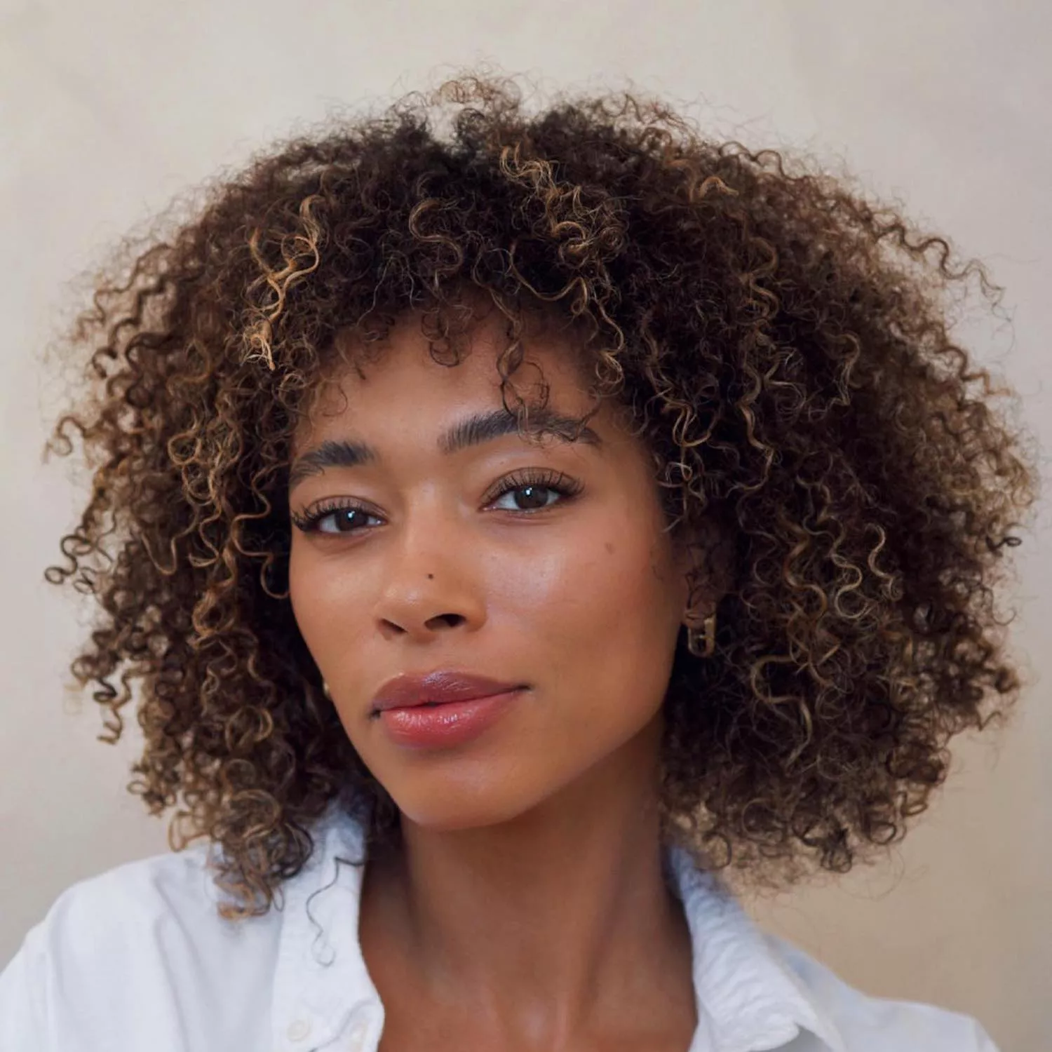 Content creator Lesley Buckle wears a naturally curly hairstyle with subtle linen blonde highlights