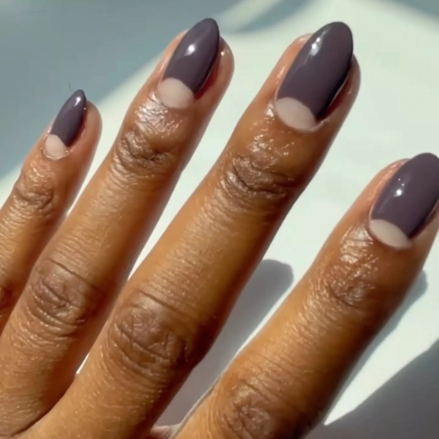 Almond-shaped manicure with dark gray polish and negative space cuticle half-moons
