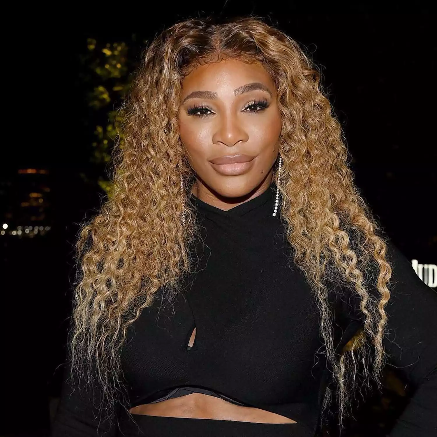 Serena Williams wears a golden beige blonde curly hairstyle and radiant makeup