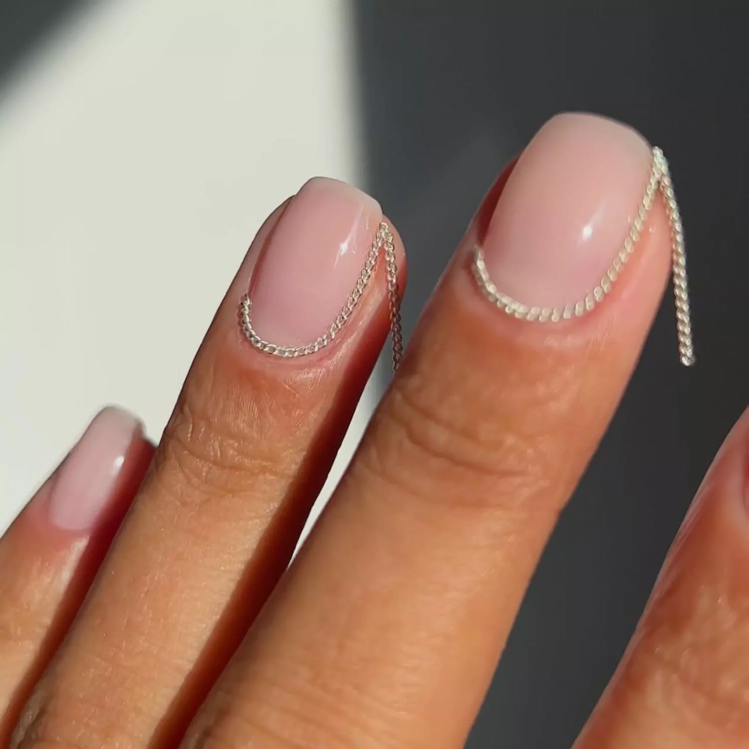 Manicure with neutral base and chain detail along cuticle with hanging end