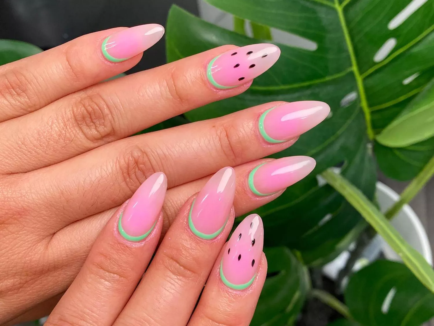 Manicure with watermelon pink base, green cuticle "rind", and black dotted seed design