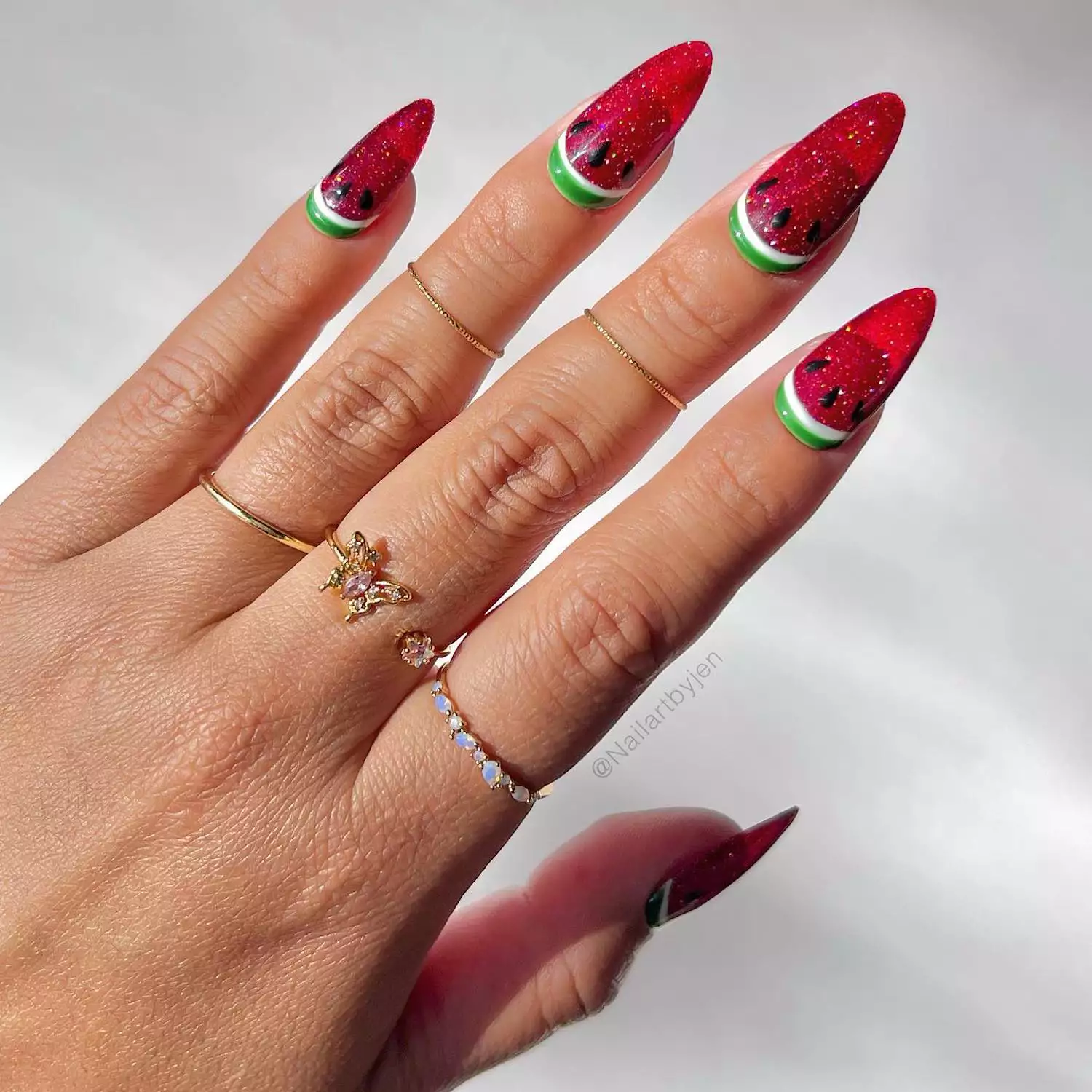Manicure with red holographic sparkle base, green cuticle watermelon "rind", and black seed design