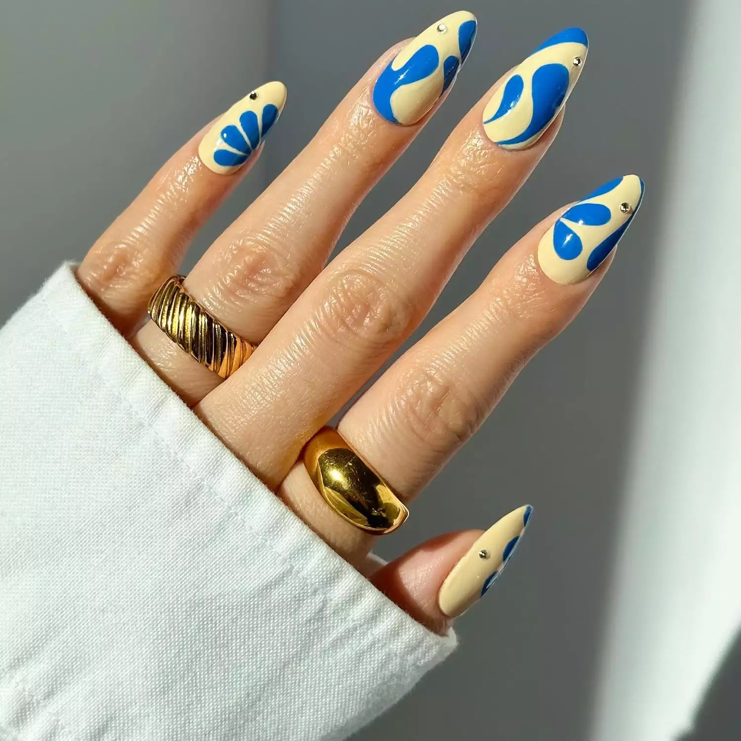 Ivory manicure with abstract cobalt blue designs and rhinestone details
