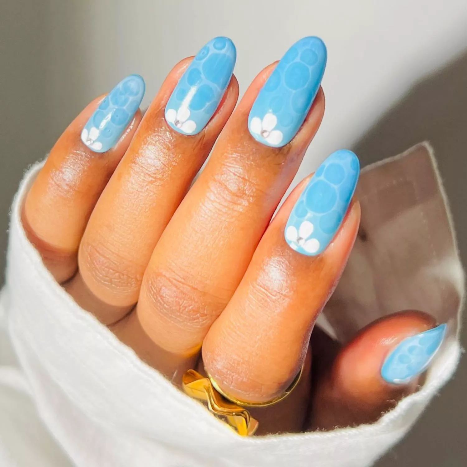 Light blue manicure with white and darker blue bubble designs and rhinestone accents