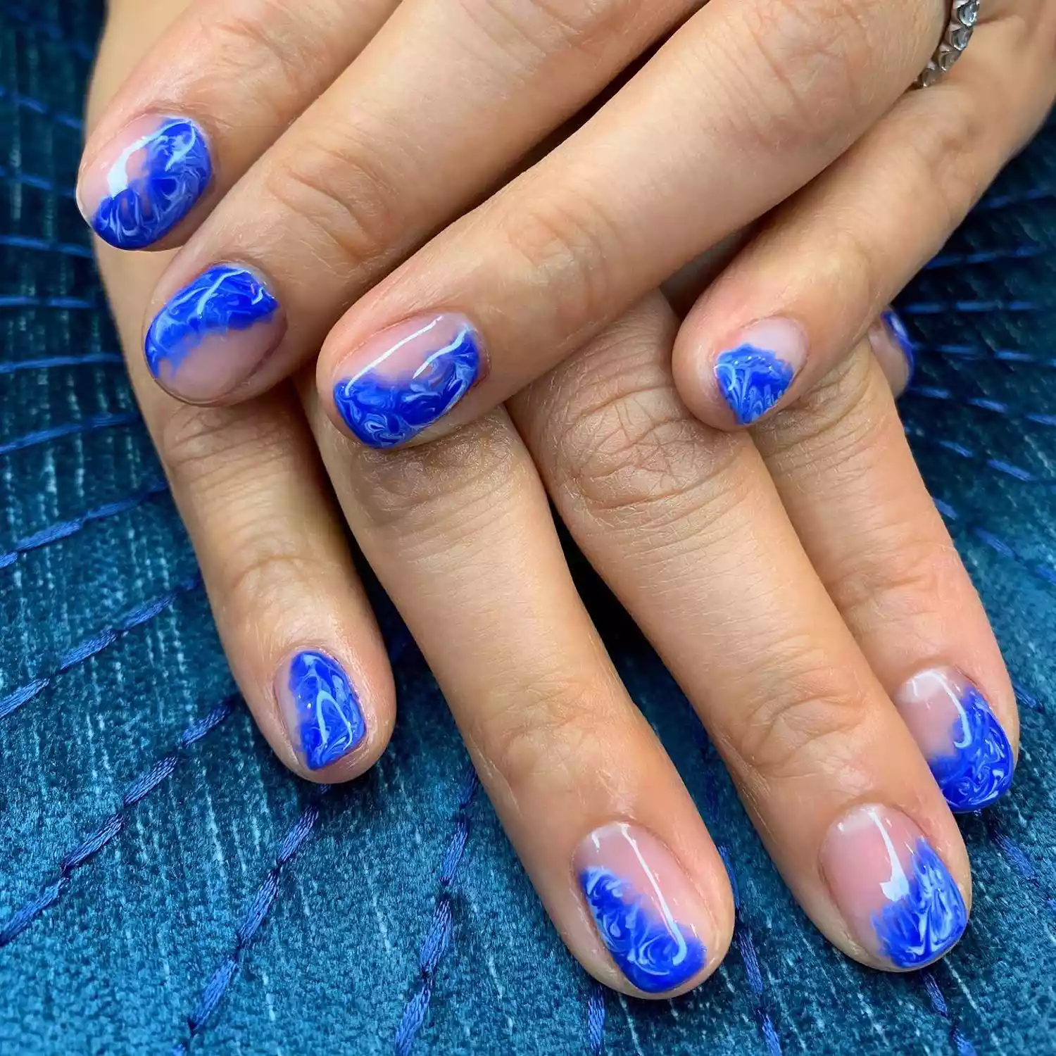 Manicure with blue and white marbled abstract wave designs on part of nails