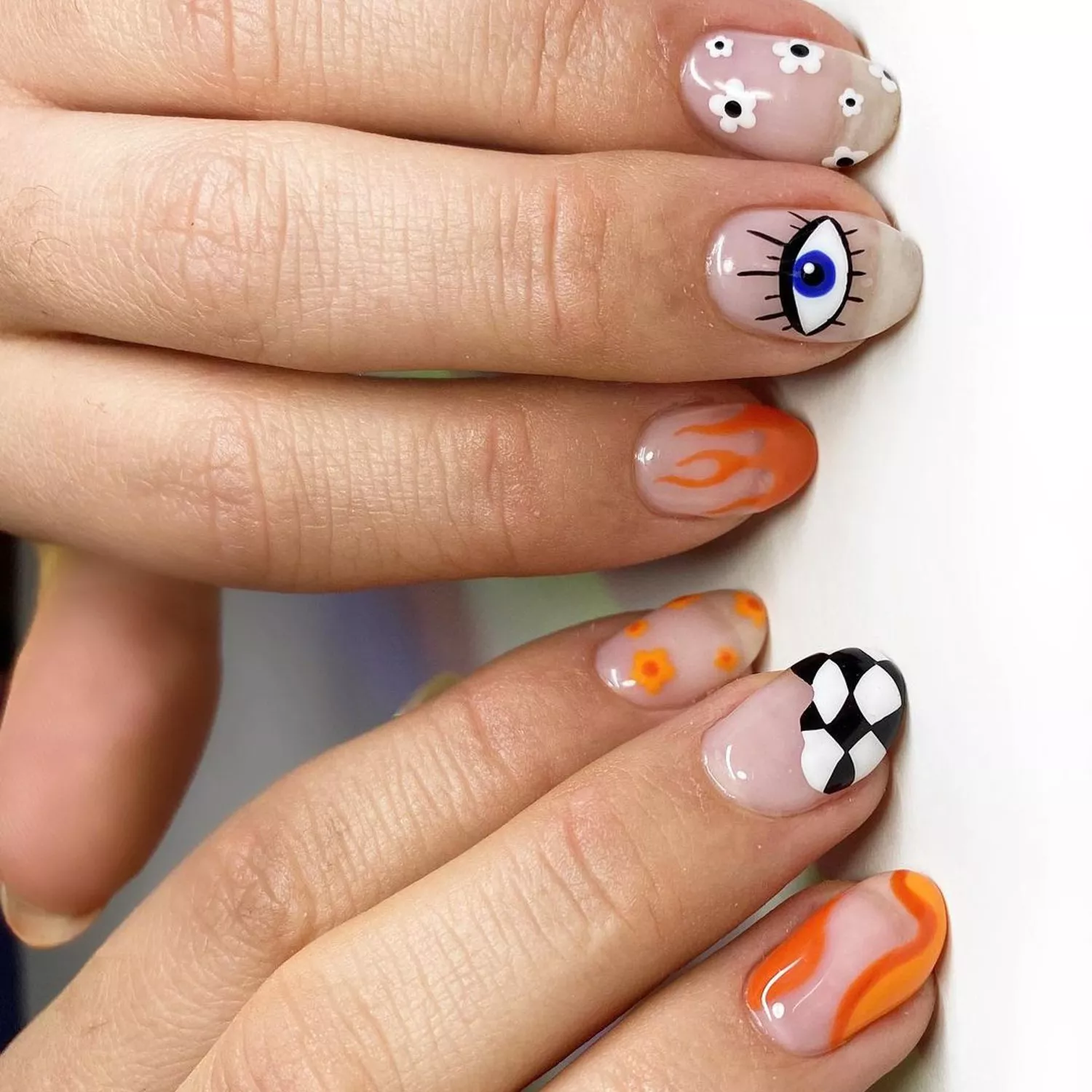 Manicure with white and orange daisy, evil eye, flame, and abstract checkerboard designs
