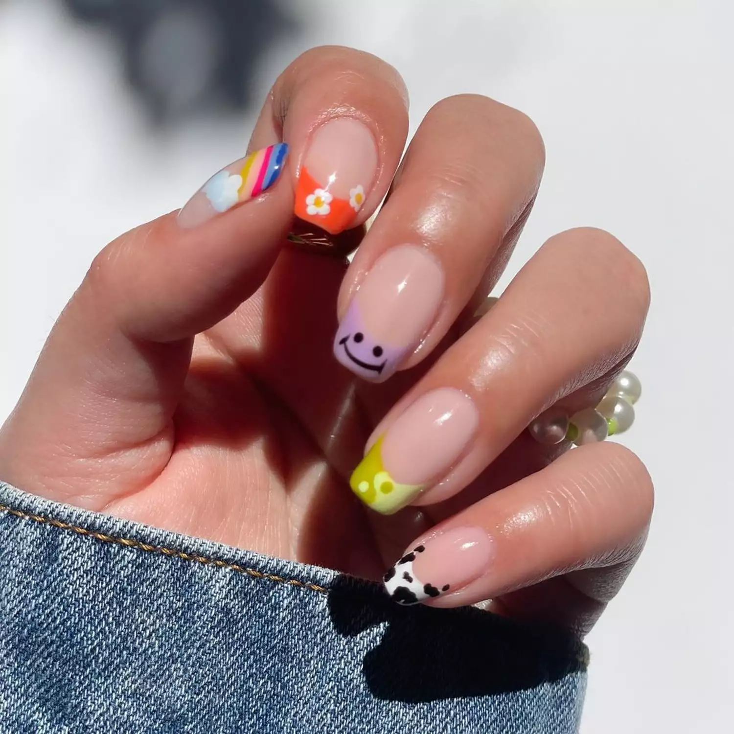French manicure with mismatched daisy, smiley face, yin/yang, rainbow, and cow print designs