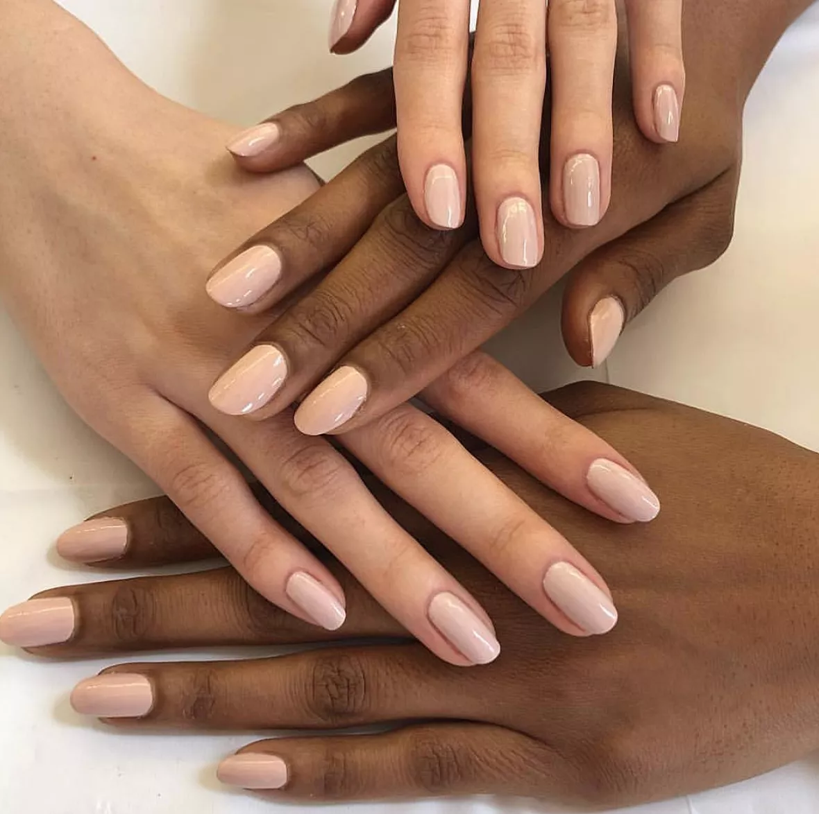 Caucasian and African American hands layered over one another, all featuring nude fingernails.