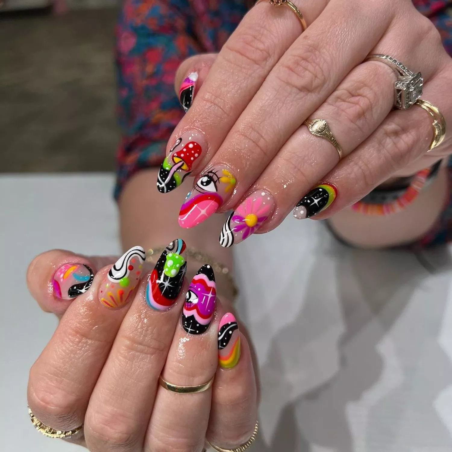 Manicure with mismatched psychedelic designs including eyes, mushrooms, flowers, and rainbows