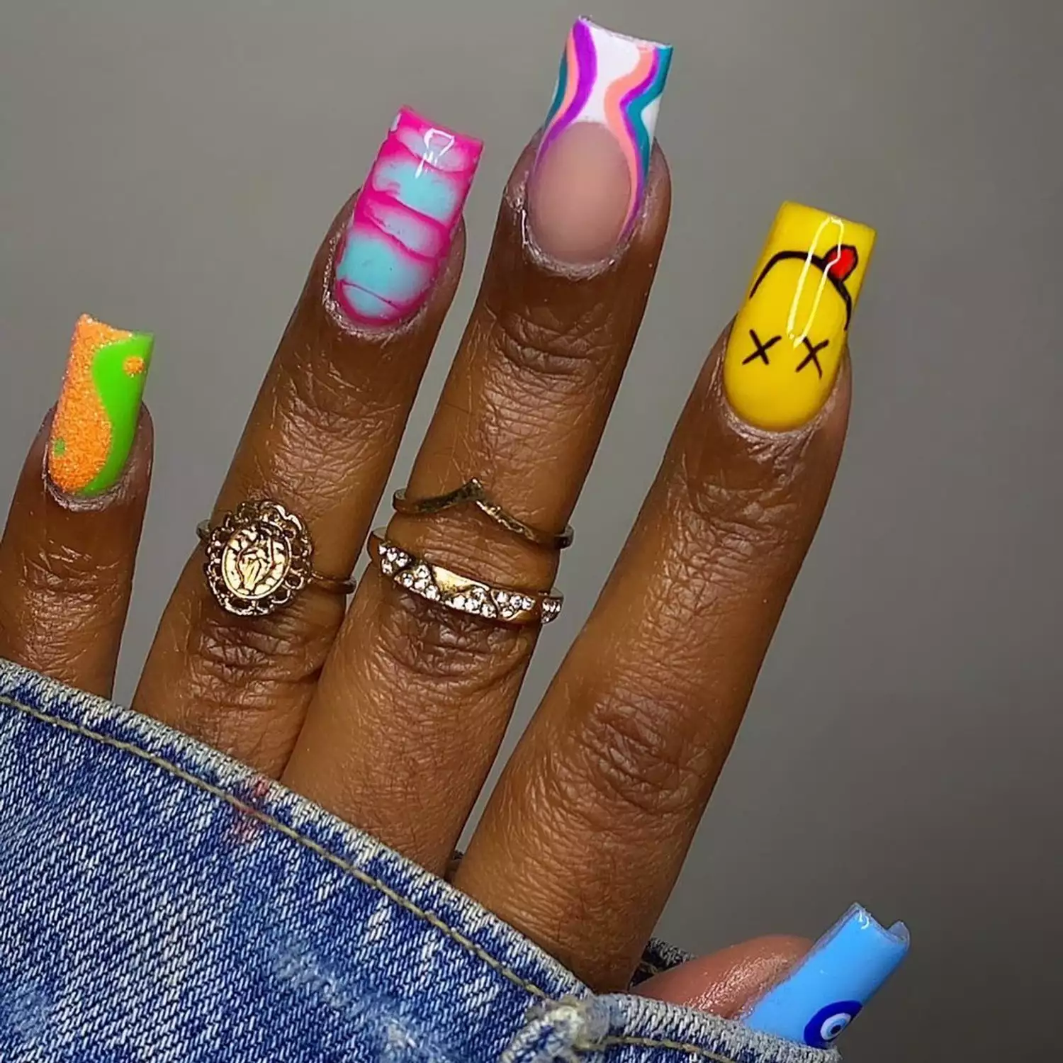 Mismatched manicure with brightly colored smiley face, wave, dye, evil eye, and yin/yang designs