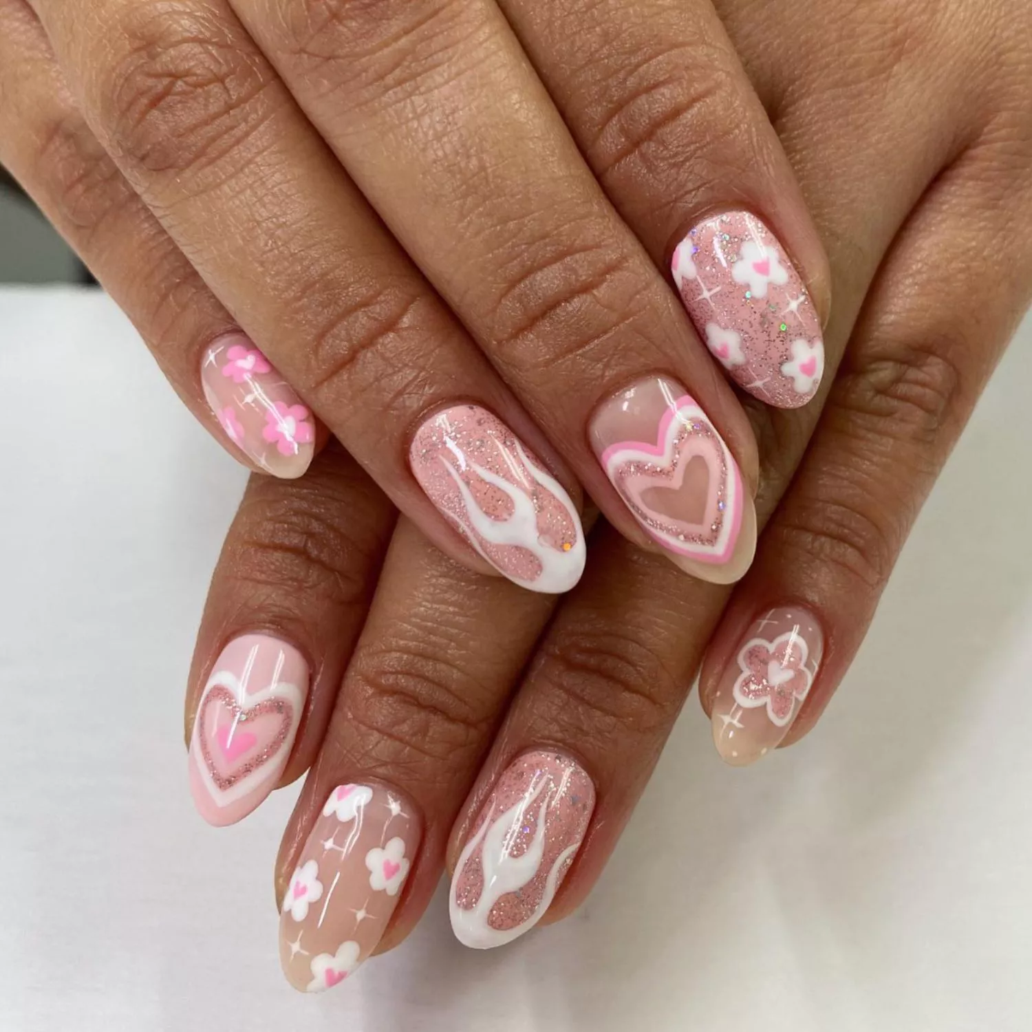 Pink and white manicure with assorted flower, flame, and heart designs