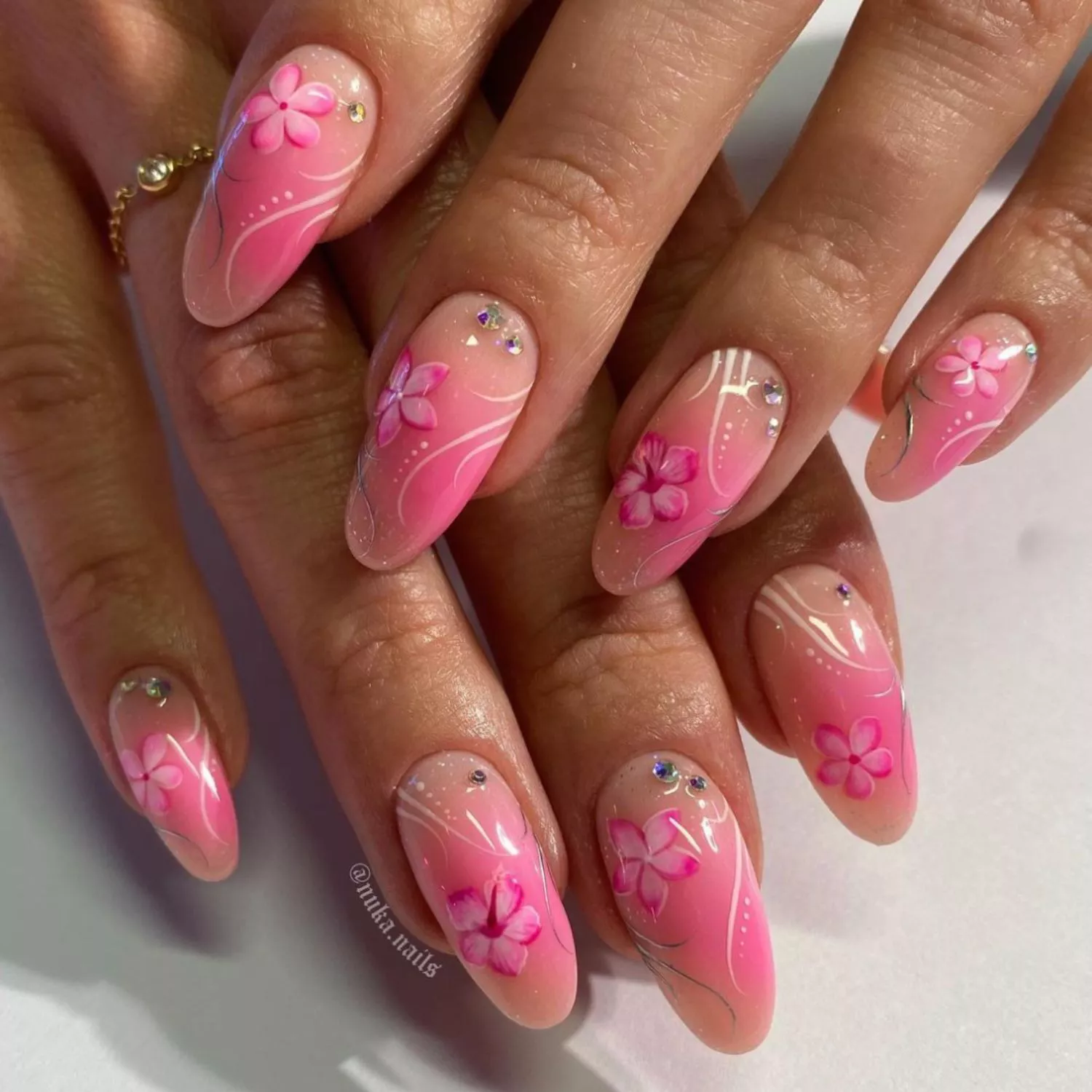 Pink ombre manicure with hibiscus designs, rhinestones, and white curving lines