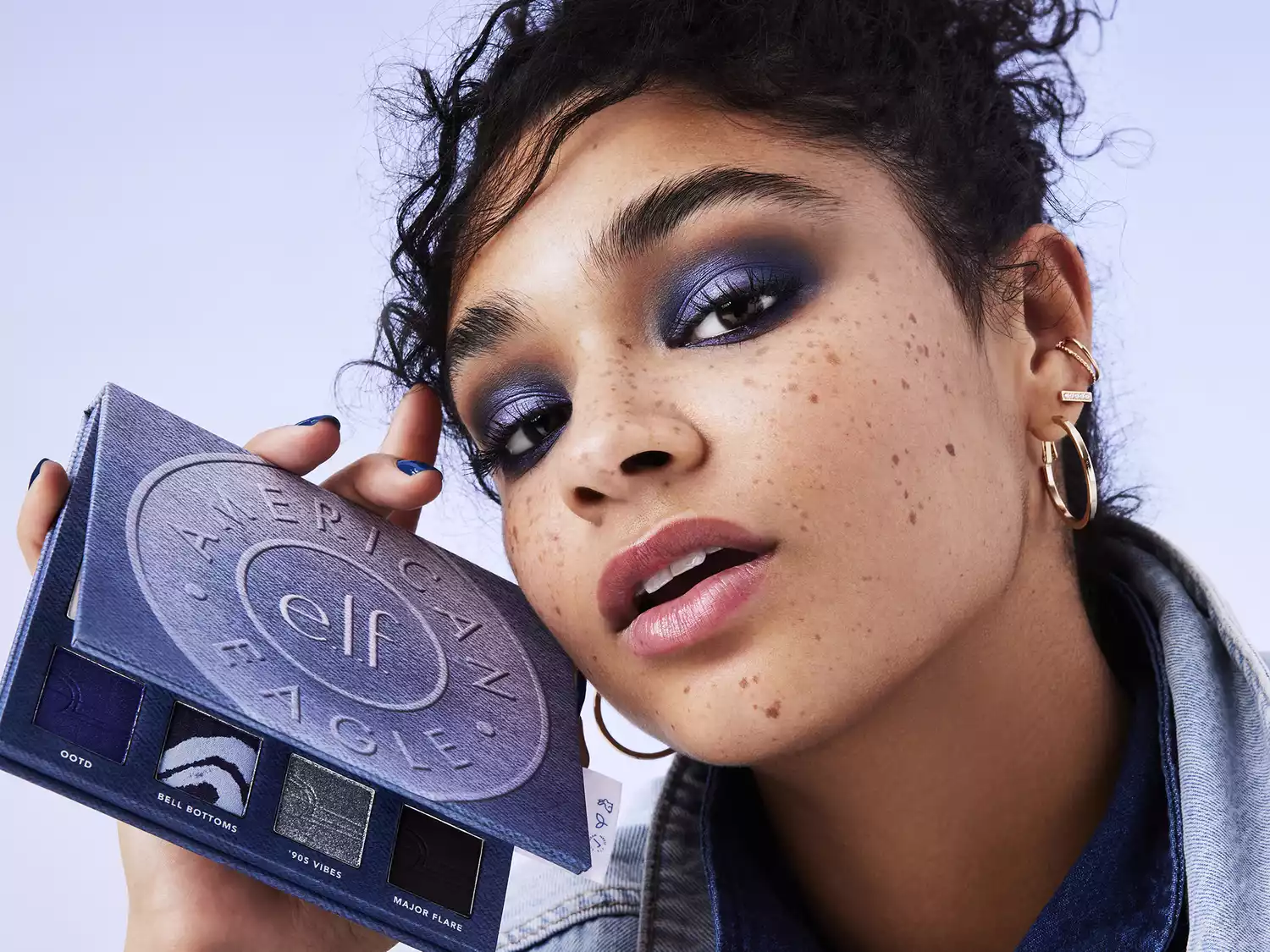 A model wearing blue eyeshadow and holding the AE x e.l.f Eyeshadow Palette