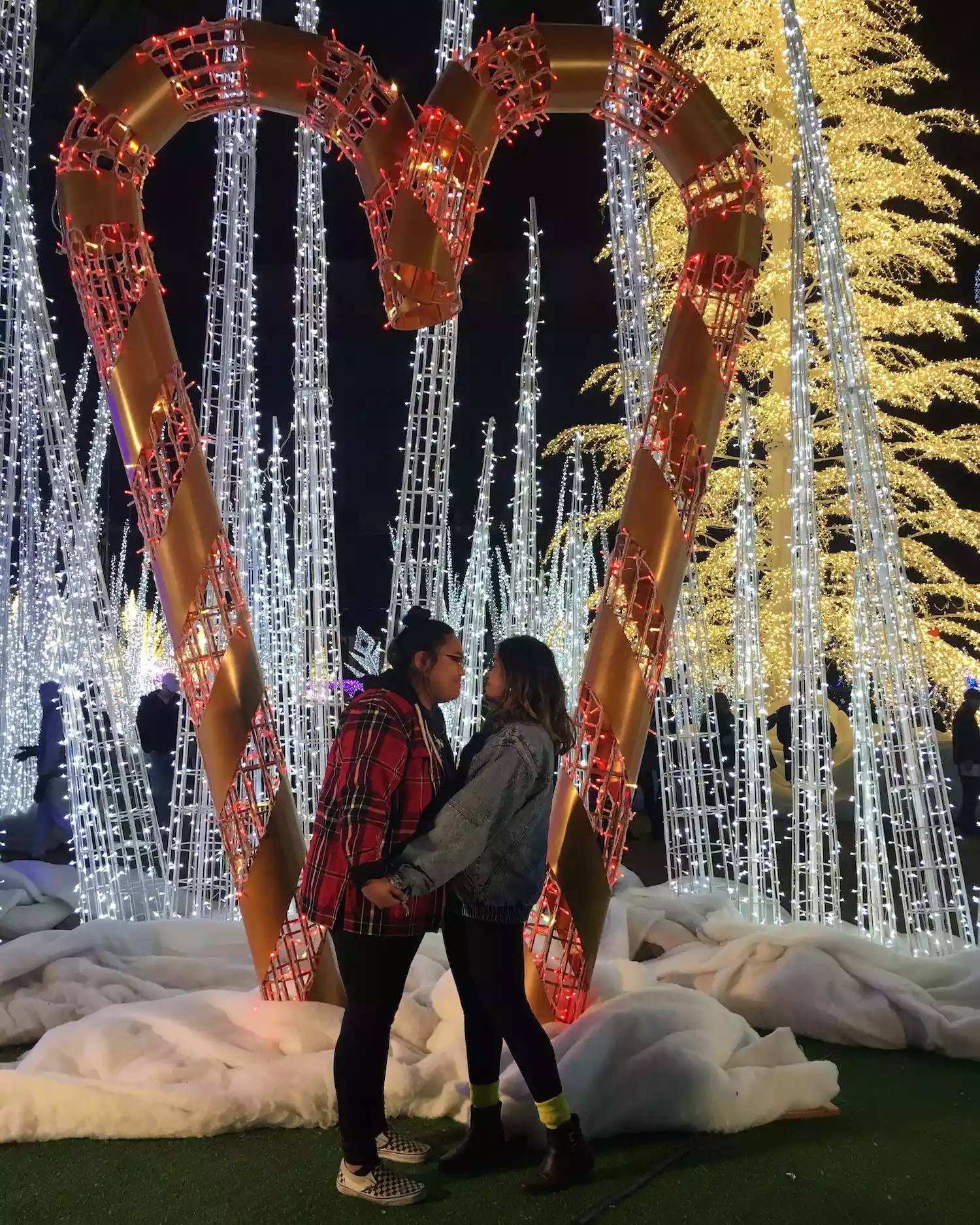 Byrdie writer Aleenah Ansari and her fiancee pose by a heart-shaped holiday lights pop-up
